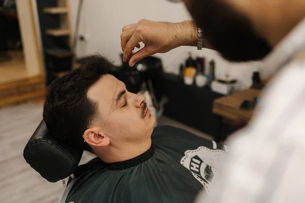 Process of threading procedure in barber shop. Professional barber correcting shape of brows with threads male client sitting in chair. High quality photo