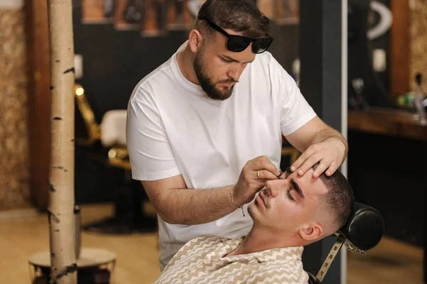 Side view of barber man trimming eyebrows with tweezers for confident man. High quality photo