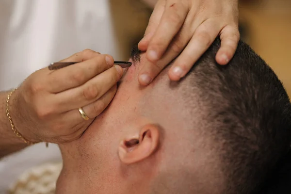 Close-up of barber man trimming eyebrows with tweezers for confident man. High quality photo