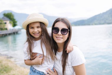 Güzel bir kız ve güzel bir annenin portresi. Gölün yanındaki açık hava fotoseti. Açık mavi su. Mutlu aile kavramı. Yüksek kalite fotoğraf