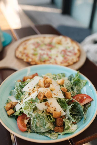 在咖啡店桌上的好吃的食物 凯撒沙拉和薄薄的披萨加培根高质量的照片 — 图库照片