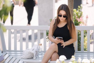 Açık havada akıllı telefon kullanan çekici genç bir kadın. Kadın bankta oturuyor ve dinleniyor. Yüksek kalite fotoğraf