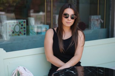 Siyah elbiseli ve gözlüklü güzel bir kızın portresi. Kadın kafede oturuyor ve garsonu bekliyor. Yüksek kalite fotoğraf