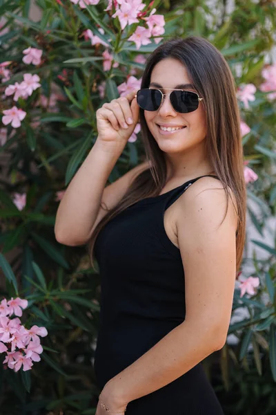 Siyah Elbiseli Gülümseyen Bayan Çiçeklerin Önünde Duruyor Güneş Gözlüklü Kadın — Stok fotoğraf
