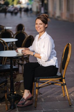 Kafede terasta kahve içen mutlu, gülümseyen kadın. Beyaz gömlekli kadın molada dinleniyor. Yüksek kalite fotoğraf