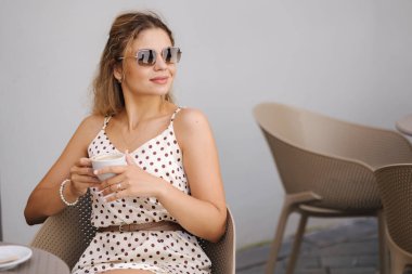 Güzel bir kadın kapuçino bardağını elinde tutuyor ve terastaki kafede oturuyor. Yüksek kalite fotoğraf