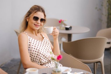 Güzel bir kadın kapuçino bardağını elinde tutuyor ve terastaki kafede oturuyor. Yüksek kalite fotoğraf