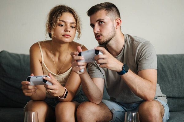 Handsome boy with his fiancee playing video games using joysticks. Man teaches her girlfriend how to play console. High quality photo