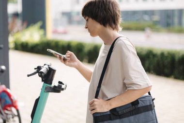 Genç çocuk onu kullanmak için kiralık elektrikli scooter 'ın QR kodunu tarıyor. Evlat hemen üniversiteye git. Yüksek kalite fotoğraf