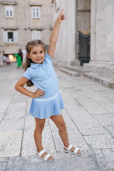 Cute five year old girl in blue dress walking in old town. Happy kid outdoor in city. High quality photo