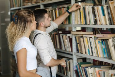 Adam kitap rafından kız arkadaşına göstermek için kitap alıyor. Üniversite kütüphanesinde sınıf arkadaşıyız. Yüksek kalite fotoğraf