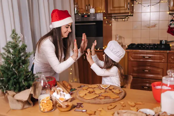 Mom in santas hat with her little doughter decorates gingerbread at home. Christmas and New Year traditions concept. Christmas bakery. Happy hollidays.