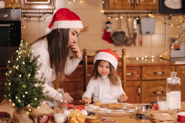 Anne ve kızının evde pişirme süreci. Noel kurabiyelerini ahşap masada pişirmek için çiğ hamur. Akşam vakti mum ışığı..