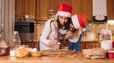 Noel tatilinde annesiyle birlikte mutfakta çok tatlı küçük bir kız. Masadaki dekoratif uygun ağaç. Kızlar zencefilli ekmek yapar..