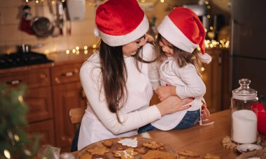 Noel tatilinde annesiyle birlikte mutfakta çok tatlı küçük bir kız. Masadaki dekoratif uygun ağaç. Kızlar zencefilli ekmek yapar..