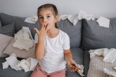 Sevimli ve güzel küçük kız çikolata yiyor ama ellerinde eriyor, o yüzden kız parmaklarını yalıyor. Yüksek kalite fotoğraf