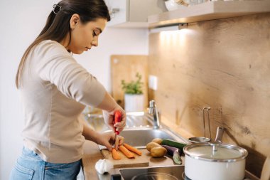 Close-up of female hand using knife and cutting carrot on wooden table. Home food concept . High quality photo
