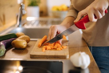 Close-up of female hand using knife and cutting carrot on wooden table. Home food concept . High quality photo