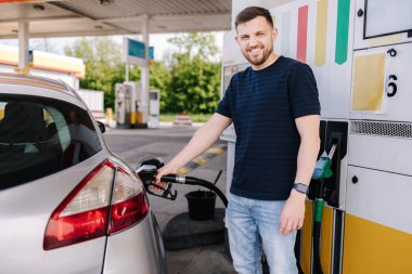 Sakallı adam benzin istasyonunda arabasına yakıt dolduruyor ve akıllı telefonuna bakıyor. İnsanoğlu yakıt fiyatlarını karşılaştırır. Yüksek kalite fotoğraf