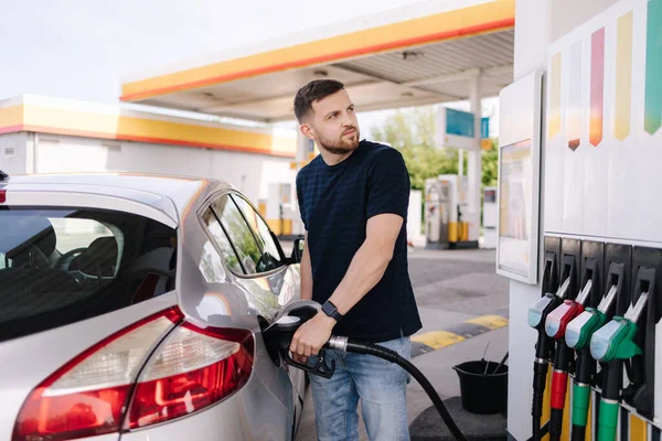 Bearded man refuelling car on gas station and looking into his smartphone. Man compares fuel prices . High quality photo