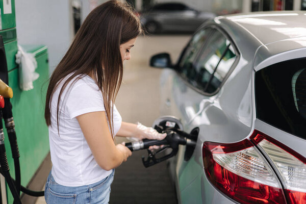 Attractive young woman refueling car at gas station. Female filling diesel at gasoline fuel in car using a fuel nozzle. Petrol concept. Side view.