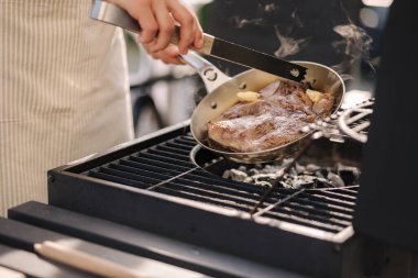 Profesyonel açık hava ızgarası. Kızartma tavasında biftek hazırlayan erkek şefin yakın çekimi. Yüksek kalite fotoğraf