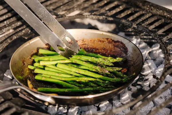 Close-up of healthy frying green asparagus with butter and garlic on carbon steel frying pan. Outdoor BBQ grill. High quality photo