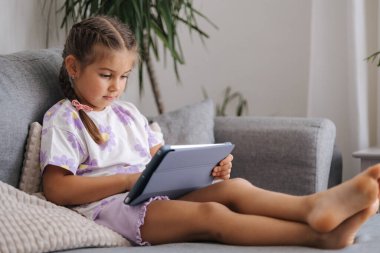 Sevimli küçük kız evde tablet kullanıyor. Beş yaşındaki kız tabletle oyun oynuyor. Yüksek kalite fotoğraf