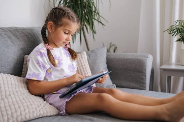 Sevimli küçük kız evde tablet kullanıyor. Beş yaşındaki kız tabletle oyun oynuyor. Yüksek kalite fotoğraf