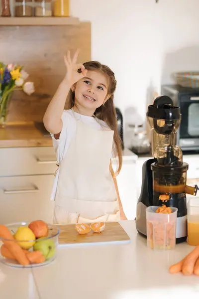 Portrait of cute five year old girl in apron preparing organic fruits and vegetables for fresh juice. Homemade vegan beverage from juicer. High quality photo