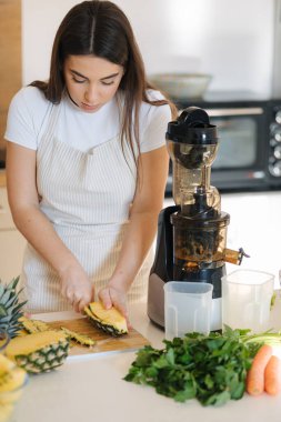 Genç bir kadın ahşap masada ananas soyar. Ev yapımı meyve suyu için meyve hazırlıyorum. Vejetaryen içeceği. Yüksek kalite fotoğraf