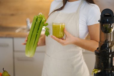 Mutfakta genç ve güzel bir kadının portresi var. Kadın elinde yeşil, sağlıklı bir içecek bardağı tutuyor. Detoks diyeti. Ev yapımı meyve suyu. Yüksek kalite fotoğraf