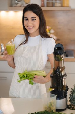 Mutfakta genç ve güzel bir kadının portresi var. Kadın elinde yeşil, sağlıklı bir içecek bardağı tutuyor. Detoks diyeti. Ev yapımı meyve suyu. Yüksek kalite fotoğraf