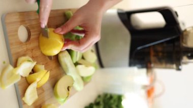 Kadın evde detoks içeceği yapıyor. Tahta masadaki organik ürünler. Dişi, limon soyar. Elma, kivi, kereviz ve salatalık. Yüksek kalite 4k görüntü
