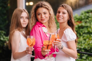 Üç kadın elinde alkollü kokteyller tutuyor ve kameraya gülümsüyor. Tavuklu tart. Aperol spreyleri. Yüksek kalite fotoğraf