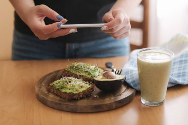 Dişi, sağlıklı kahvaltıların fotoğrafını çeker. Avokado sandviçi. Yeşil smoothie. Vejetaryen yemeği. Yüksek kalite fotoğraf