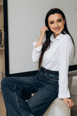 Beyaz gömlekli, resmi kot giyen, sandalyede oturan mutlu, gülümseyen kadın. Yüksek kalite fotoğraf