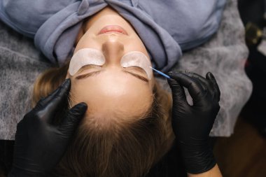 Güzellik stüdyosunda kirpik yapan bir kadın. Sarı saç modelinin kirpikleri için boyası, kıvırcığı, kaplaması ve uzantısı var. Birinci kişi görünümü.