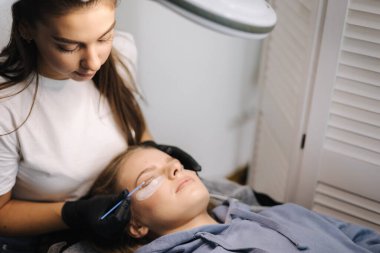 Genç manken için kirpik kaplama prosedürleri yapan bir güzellik uzmanı. Modern kirpik bakım prosedürleri laminasyon ve kirpiklerin genişletilmesi. Profesyonel güzellik salonu...