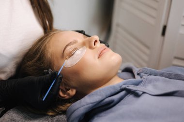 Güzellik stüdyosunda kirpik kaplama yaptıran çekici sarı saç modeli. Kırbaçlar için modern kullanışlı işlem.