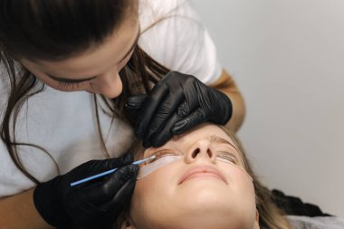 Genç manken için kirpik kaplama prosedürleri yapan bir güzellik uzmanı. Modern kirpik bakım prosedürleri laminasyon ve kirpiklerin genişletilmesi. Profesyonel güzellik salonu..