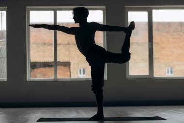 Evde esneme hareketleri yapan genç ve formda bir adamın silueti. Yogacı adam farklı egzersizler yapar. Yüksek kalite fotoğraf