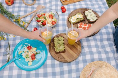 Açık hava vejetaryen pikniğinin önünde portakallı limonata tutarken çekilmiş iki el fotoğrafı. Sağlıklı gıda konsepti. Yüksek kalite fotoğraf