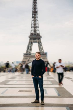 Eyfel Kulesi arka plan üzerinde duran yakışıklı adam koyu mavi kazak giyiyor.