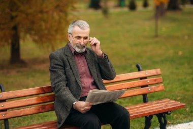 Gri ceketli güzel sakallı güzel Dede parkta bir bankta oturur ve bir gazete okuyor.