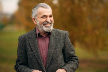 Gözlük takan yakışıklı bir yaşlı adam bir telefon kullanıyor. Sonbaharda Parkta yürümek.