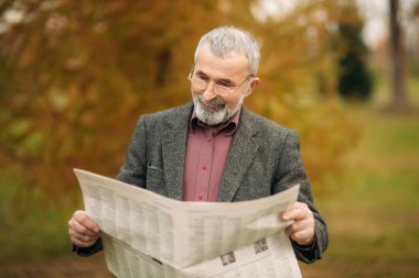 Gri ceketli güzel sakallı güzel Dede parkta bir bankta oturur ve bir gazete okuyor.