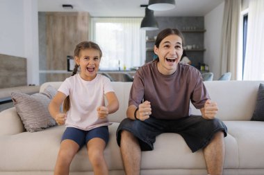 Erkek ve kız kardeş televizyon izliyor ve TV dizisindeki olaylara duygusal tepki veriyor. Genç bir oğlan ve küçük bir kız evdeki kanepede oturuyor. - Evet. Yüksek kalite fotoğraf