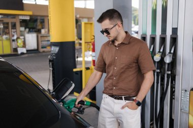 Güneş gözlüklü yakışıklı sakallı adam lüks arabasına benzin dolduruyor. Yüksek kalite fotoğraf