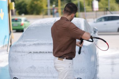 Aktif köpük kullanarak araba temizleme. Yakışıklı adam lüks arabasını oto yıkamayla yıkıyor. Yüksek kalite fotoğraf